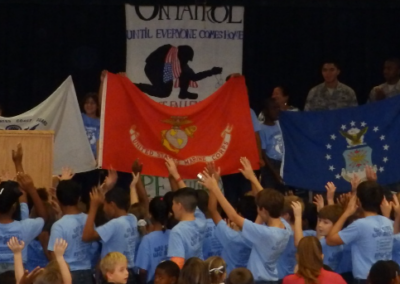 a row of kids in blue t-shirts in front of a row of flags